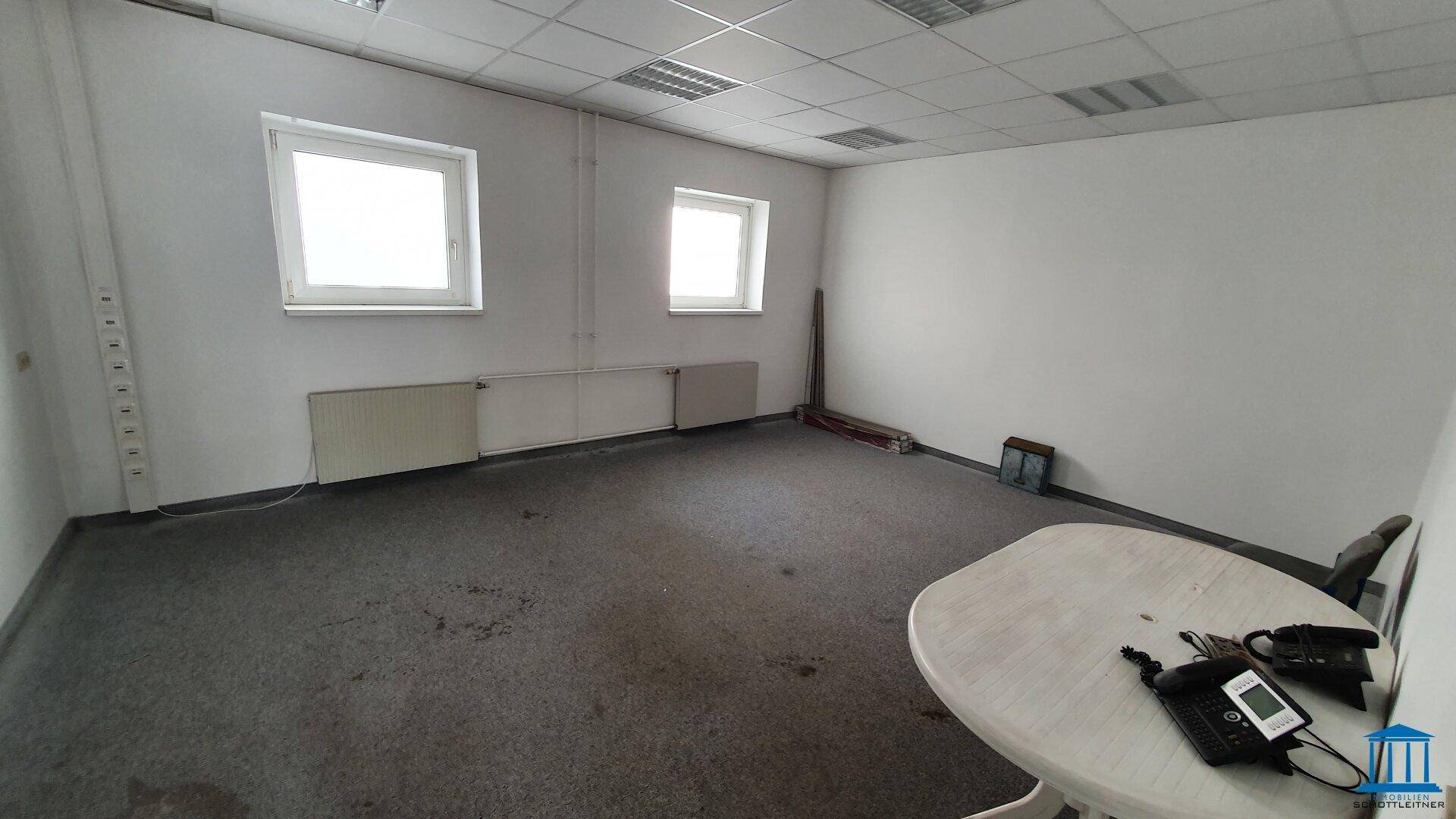 Büro mit Teppichboden, mehreren Fenstern und einem Tisch, bietet eine funktionale Arbeitsumgebung.