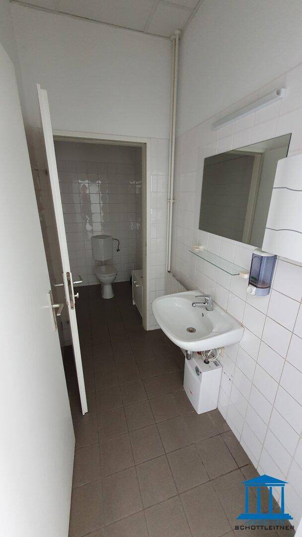 Einfache Toilette mit Waschbecken, Spiegel und weißen Fliesen, funktional und sauber.