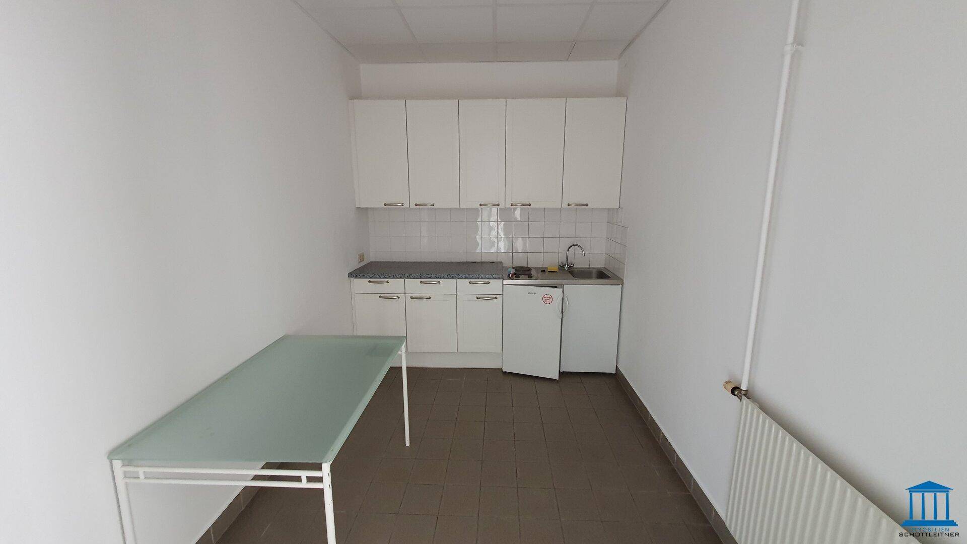 Funktionale Küchenzeile mit weißen Schränken, Spüle und kleinem Kühlschrank, ideal für Pausen.
