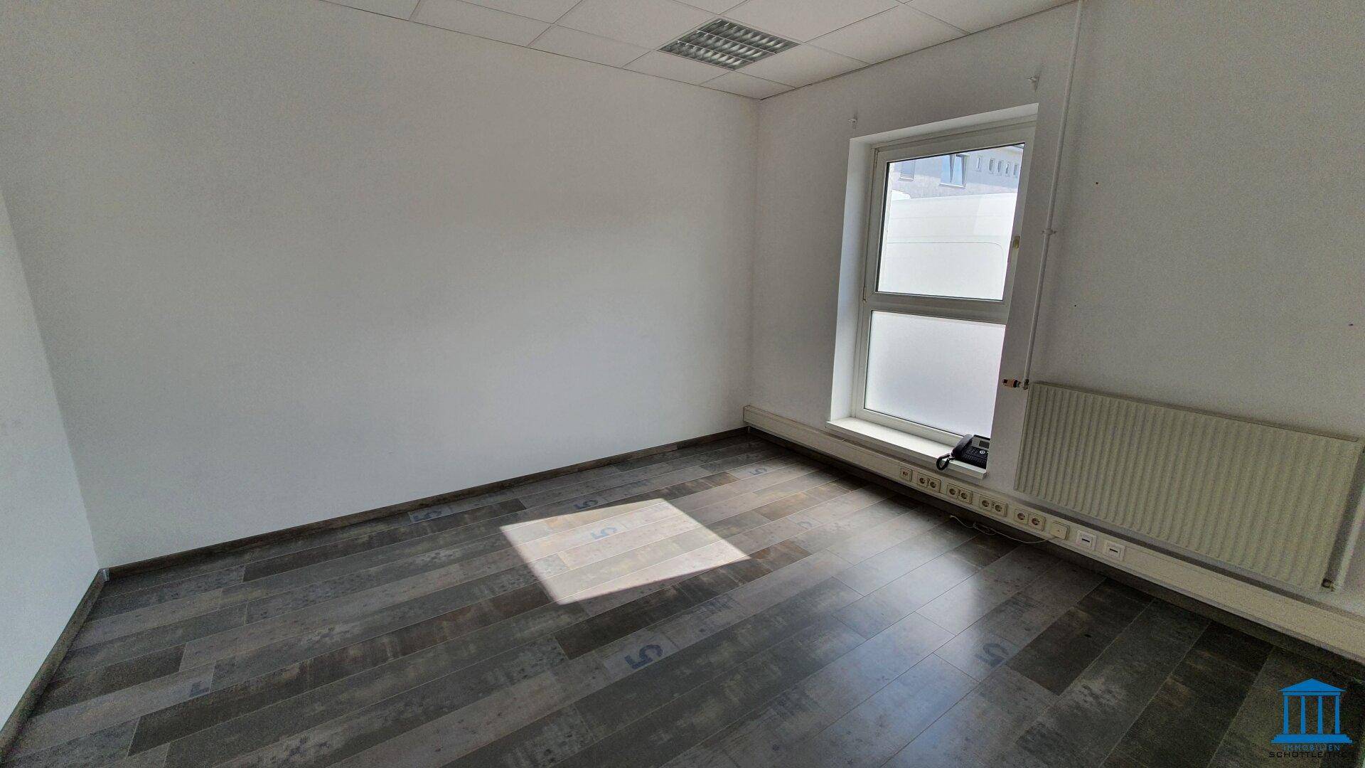 Kleineres Büro mit Laminatboden, einem Fenster und Heizkörper, ideal für Einzelarbeitsplätze.