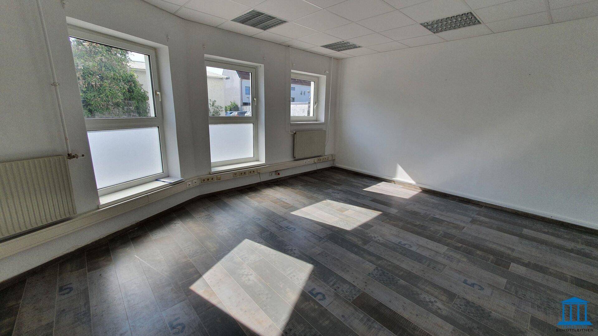 Helles Büro mit großen Fenstern, Laminatboden und Heizkörpern, bietet viel Tageslicht.