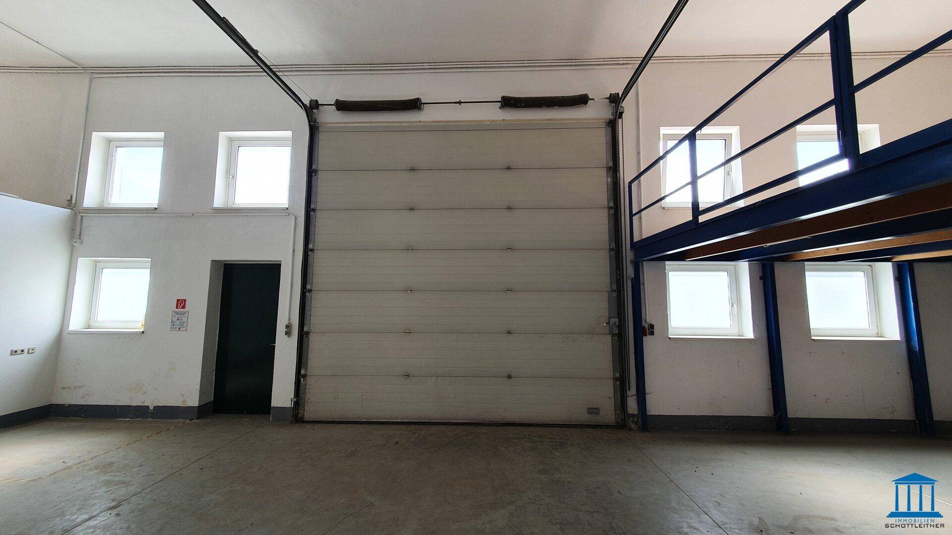 Großes Rolltor und mehrere Fenster in einem hellen Industrieraum, ideal für Anlieferungen.