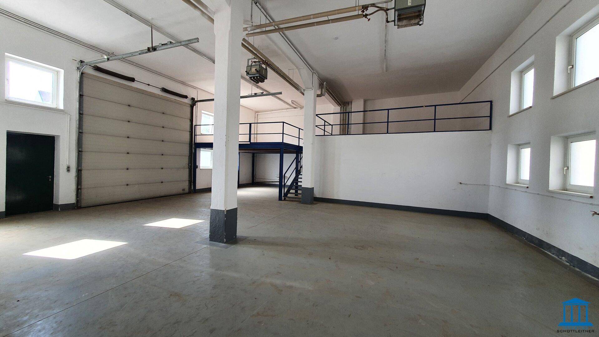 Geräumiger Lagerbereich mit Betonboden, Säulen und einer erhöhten Mezzanine-Ebene, gut beleuchtet.