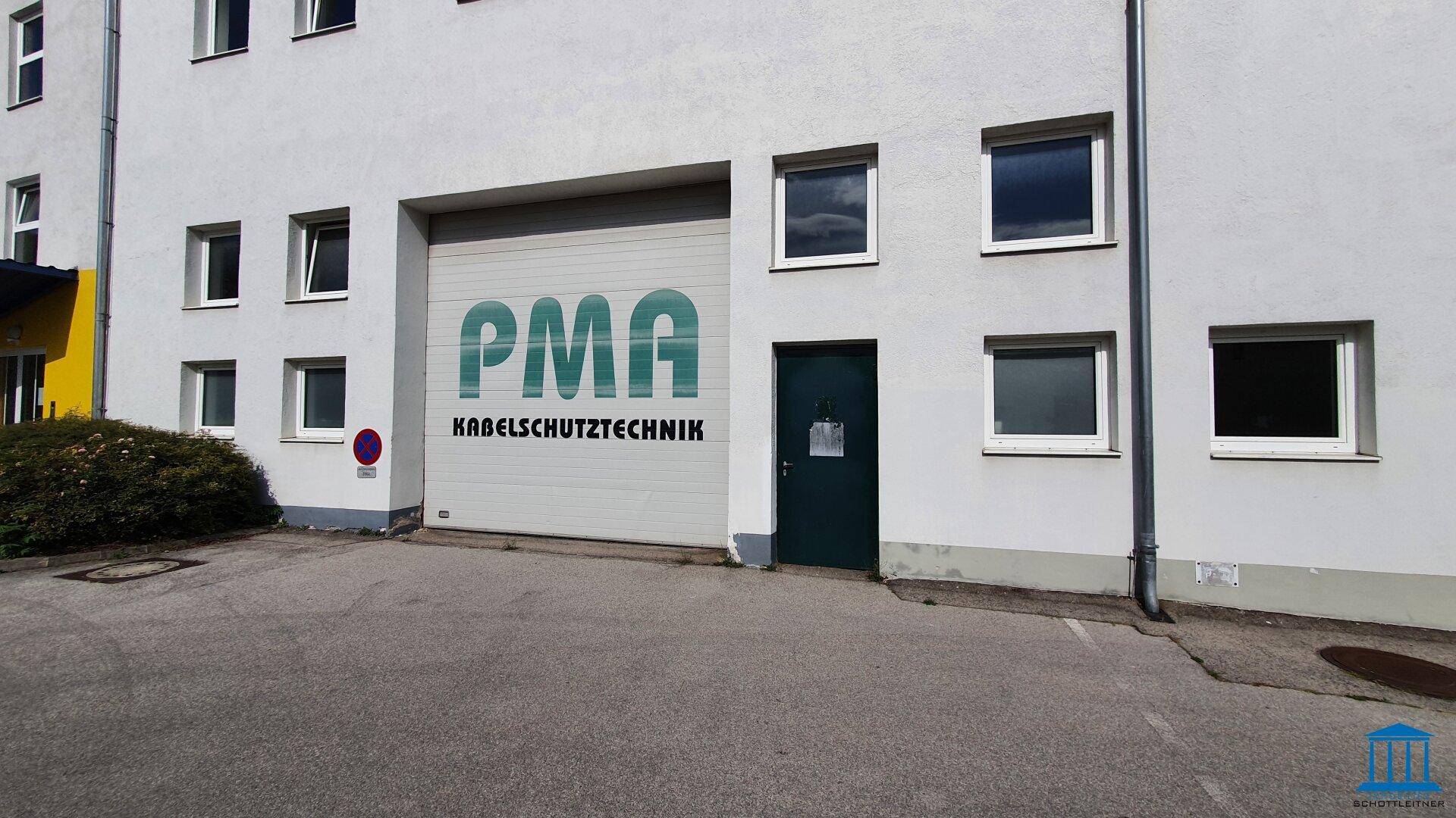 Außenansicht eines Gewerbegebäudes mit Rolltor und mehreren Fenstern, gut zugänglich.