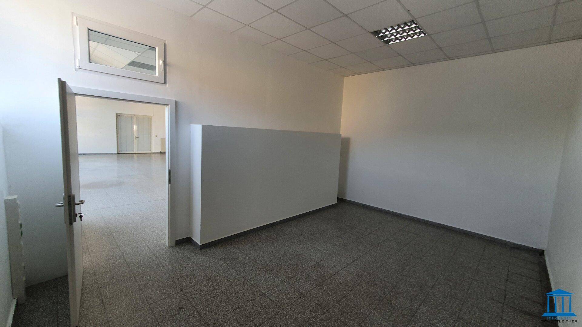 Kleinerer Raum mit Fliesenboden und einer Tür, die zu einem größeren Bereich führt, mit einem Oberlichtfenster.