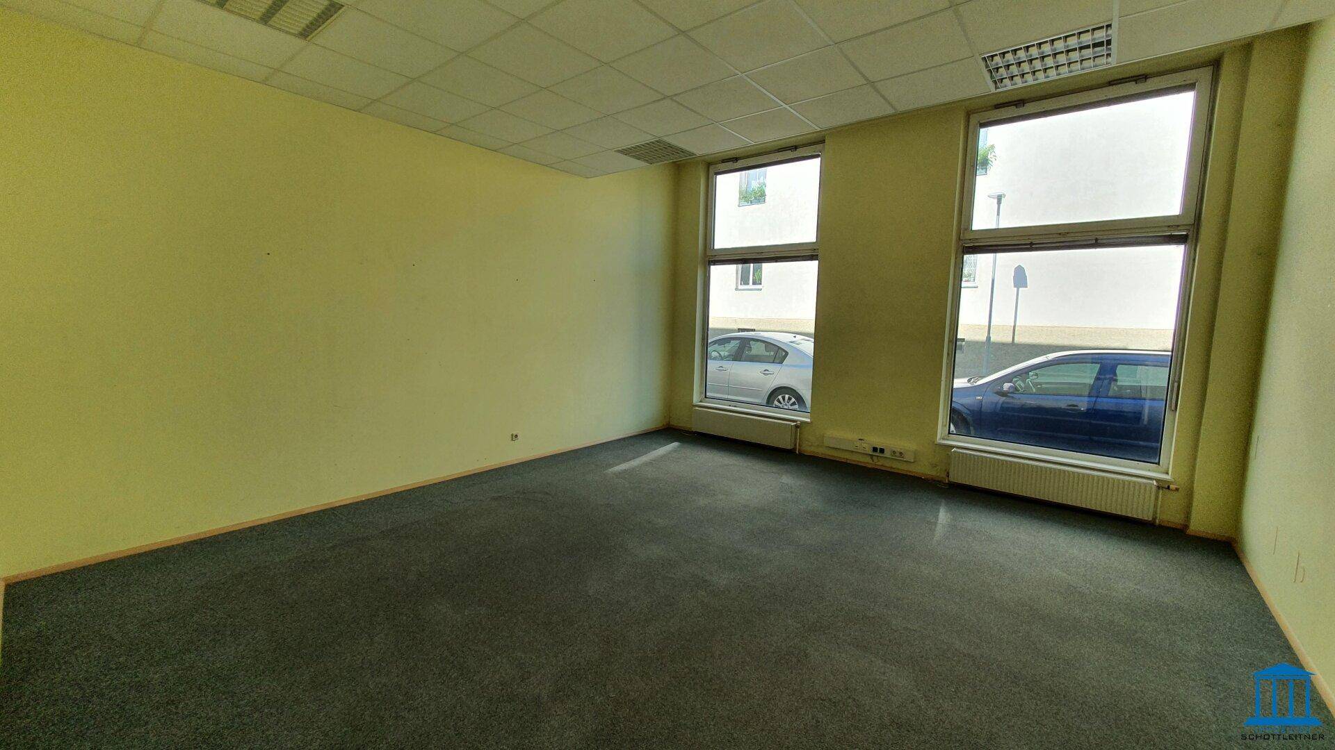 Bürofläche mit Teppichboden und zwei Fenstern zur Straße, in einem hellgelben Farbton gestrichen.