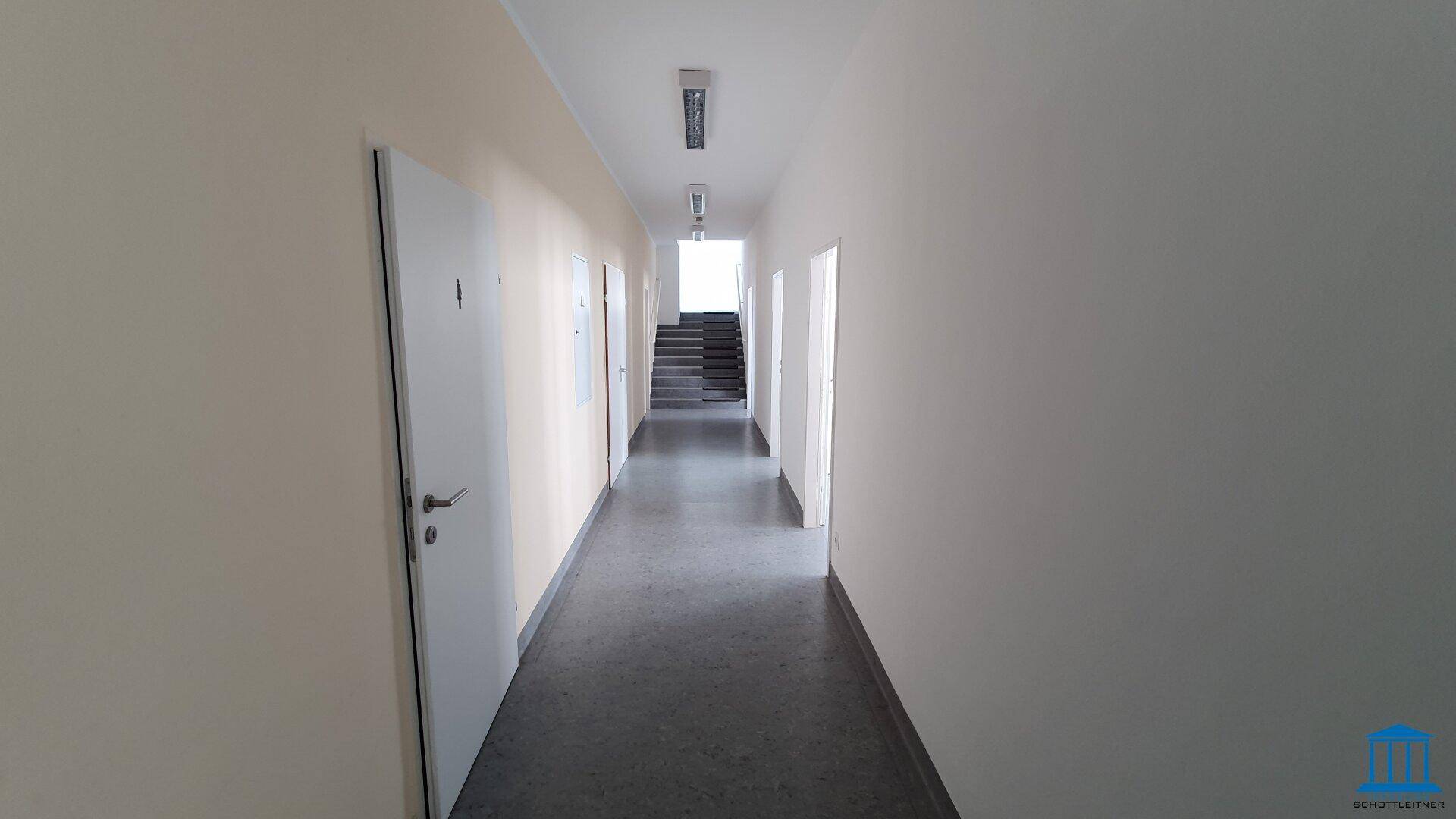 Langer Flur mit mehreren Türen und Treppenhaus am Ende, ausgestattet mit Linoleumboden.