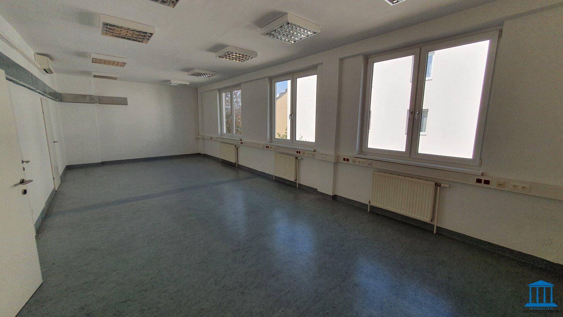 Leerer Büroraum mit mehreren Fenstern, Heizkörpern und grauem Boden, bereit für individuelle Einrichtung.