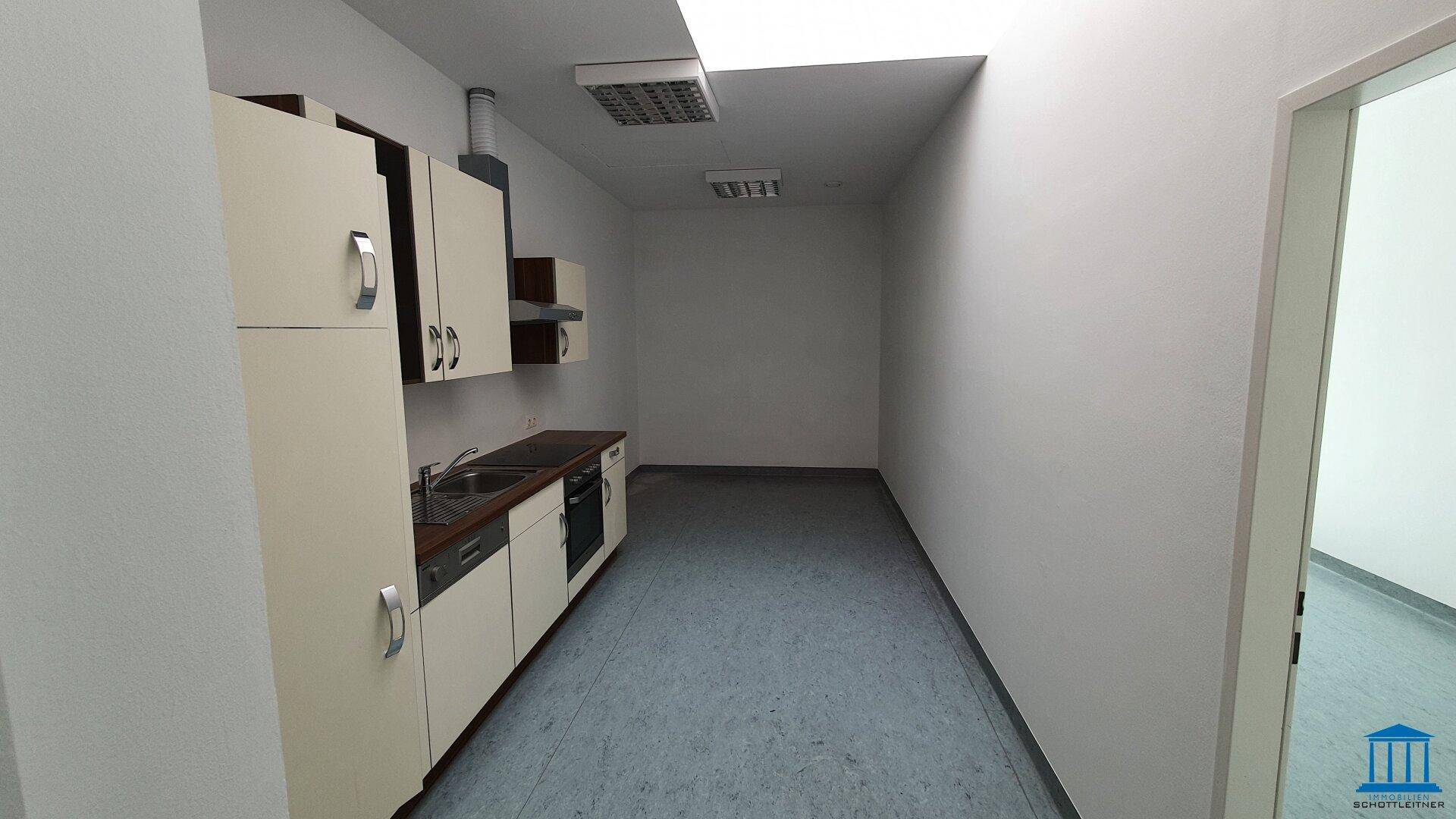 Schmale Küchenzeile mit Spüle, Herd und Hängeschränken, ideal für eine kleine Büroküche.