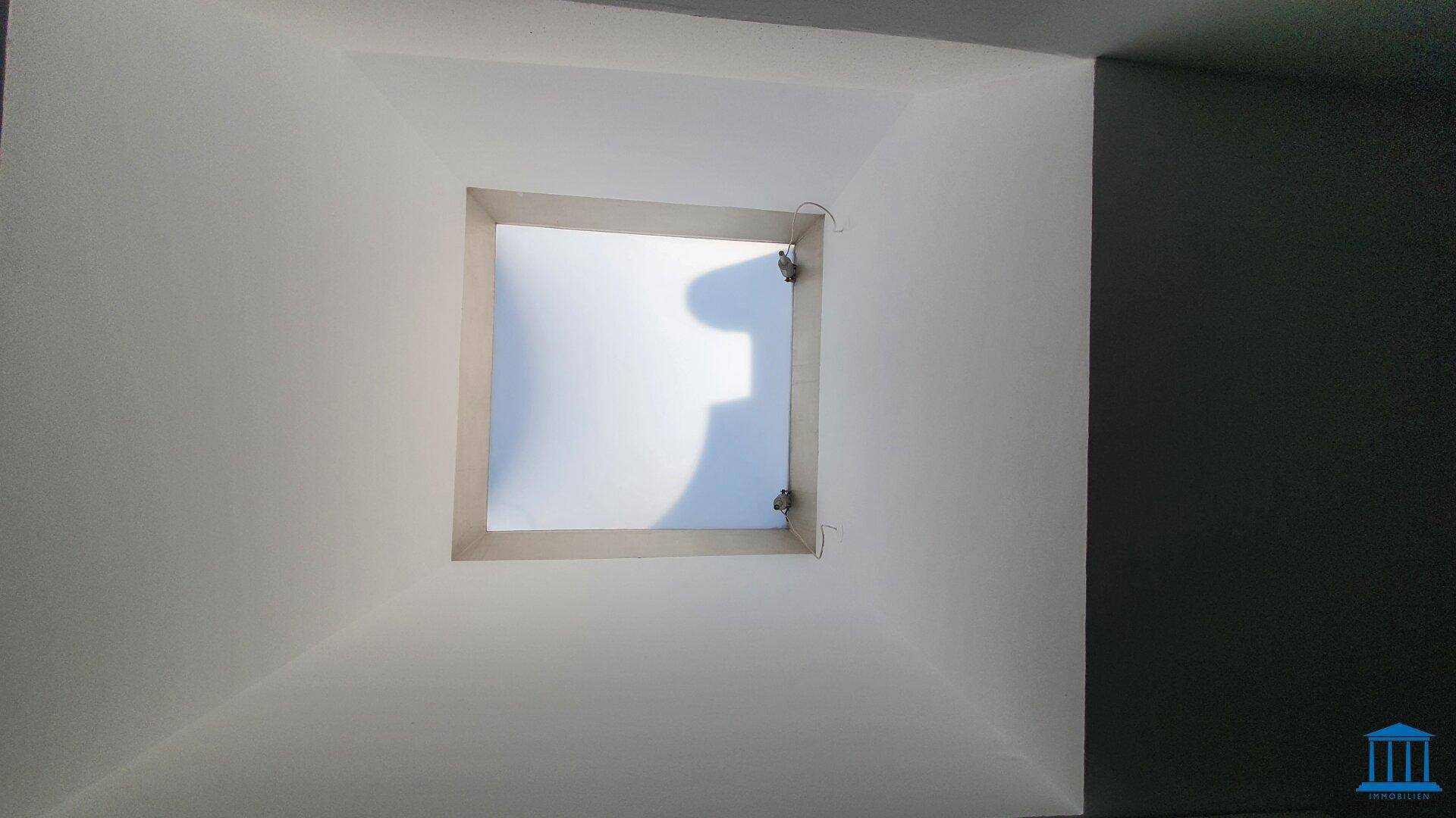 Innenraum mit einem Oberlicht, das Tageslicht hereinlässt, möglicherweise ein Flur oder Abstellraum.
