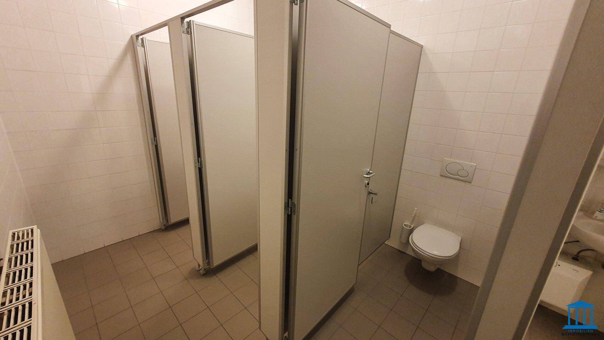 Mehrere Toilettenkabinen in einem öffentlichen Badezimmer, ausgestattet mit Fliesenboden.