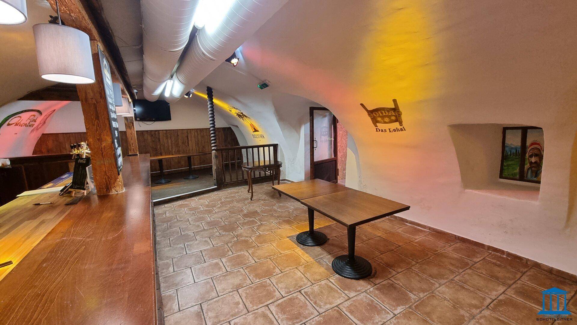 Sitzbereich mit gewölbten Decken, Fliesenboden und einem Wandgemälde, beleuchtet mit farbigem Licht.