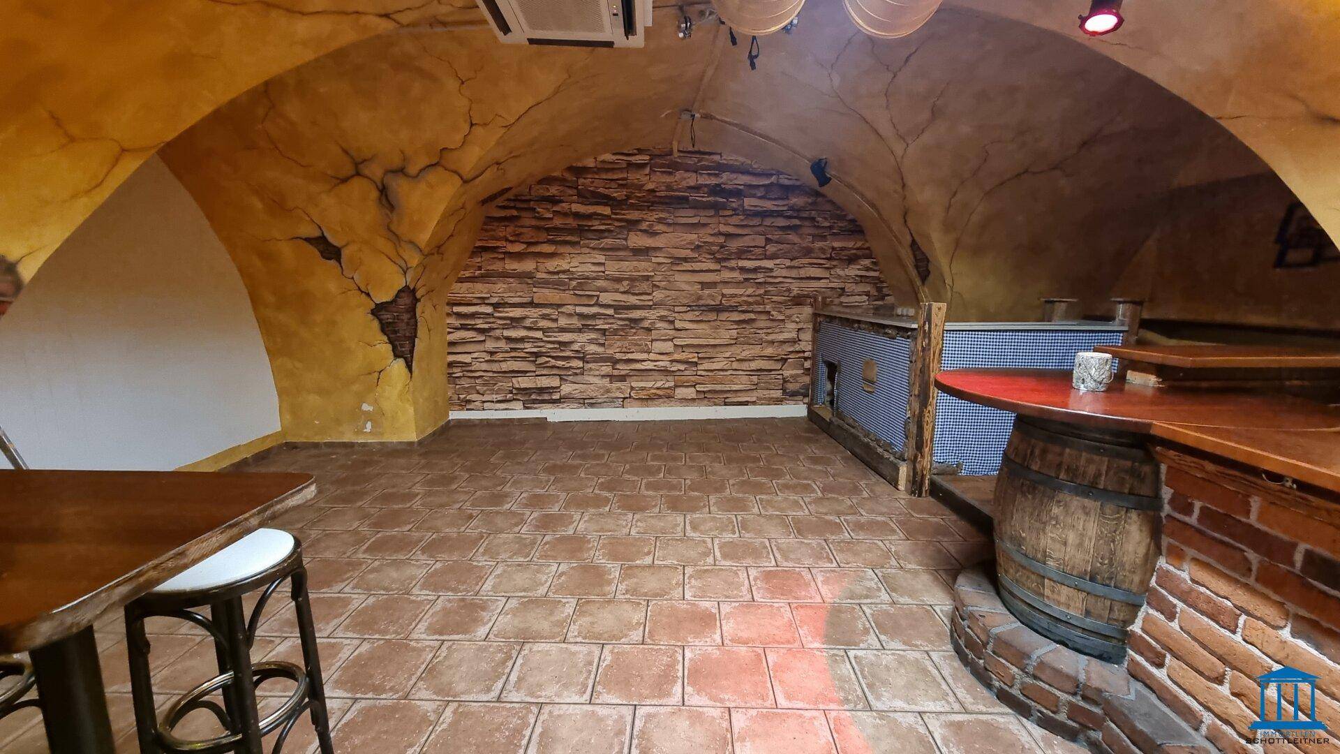 Innenansicht eines Barbereichs mit gewölbten Decken, Fliesenboden und einer markanten Steinwand im Hintergrund.