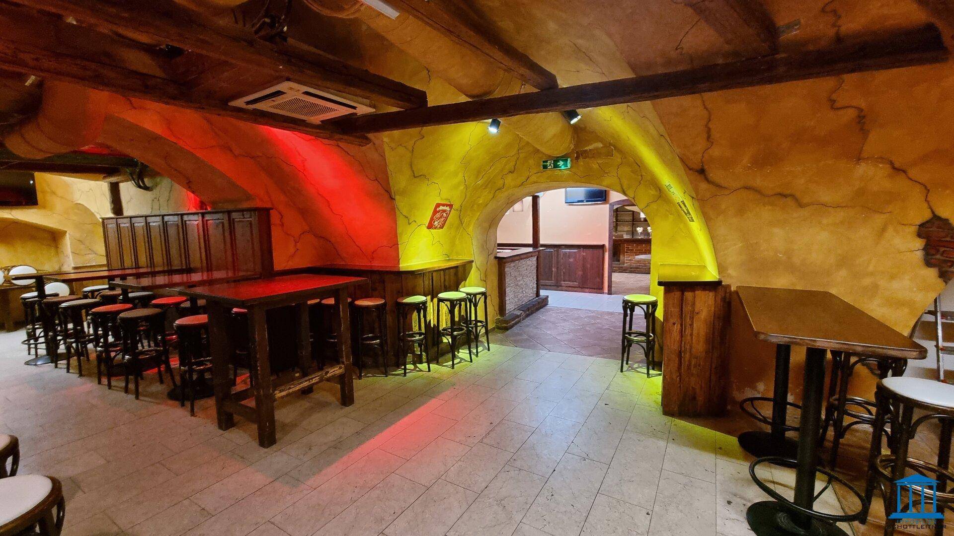 Weitläufiger Barbereich mit gewölbten Decken, Holzbalken und verschiedenen Sitzbereichen, beleuchtet mit farbigem Licht.