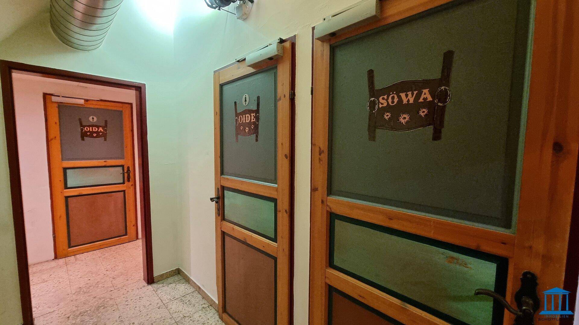 Flur mit zwei Holztüren, die zu den Toiletten führen, mit traditionellen Beschriftungen.