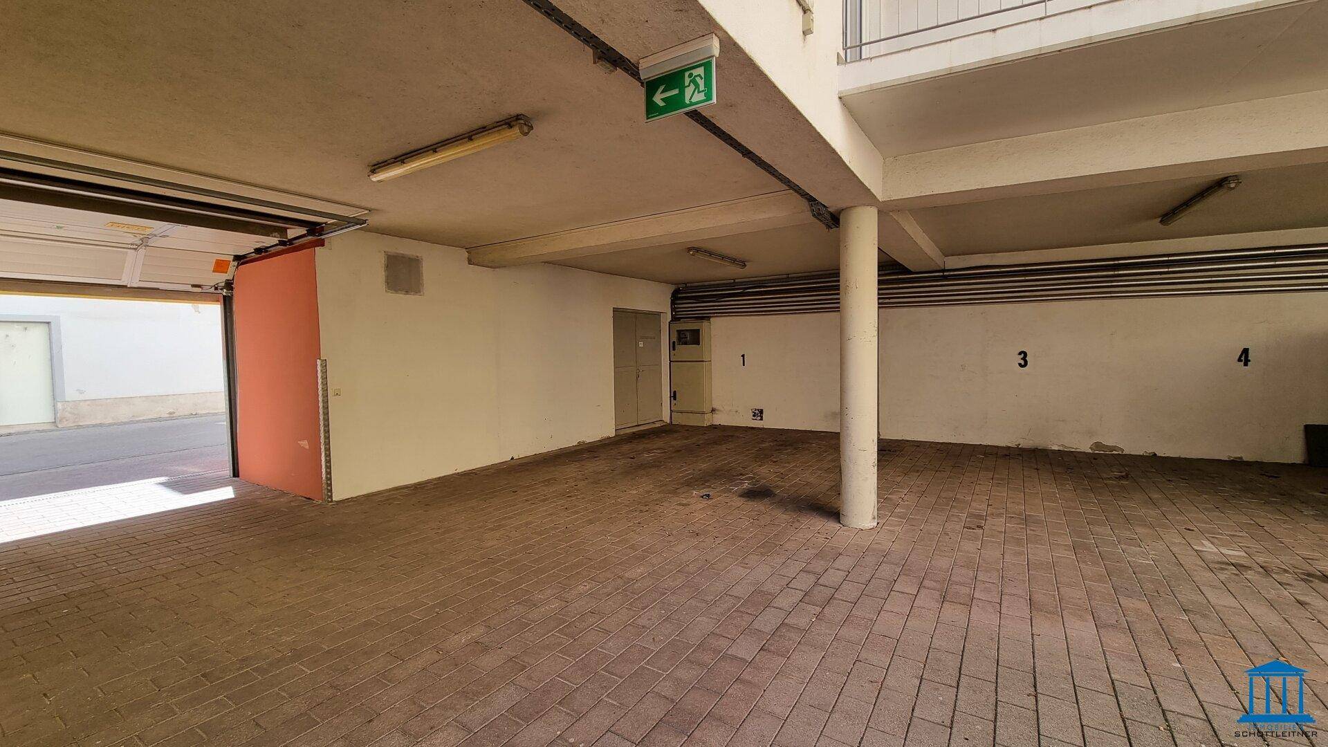 Geräumige Tiefgarage mit Betonpfeilern und gefliestem Boden, mit Ausfahrt ins Freie.