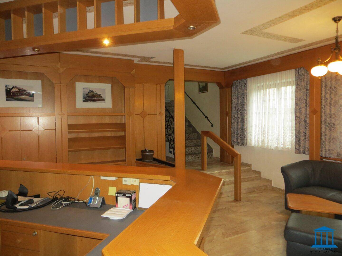 Empfangsbereich mit Holztheke, Treppenzugang und Sitzgelegenheiten in traditionellem Stil.