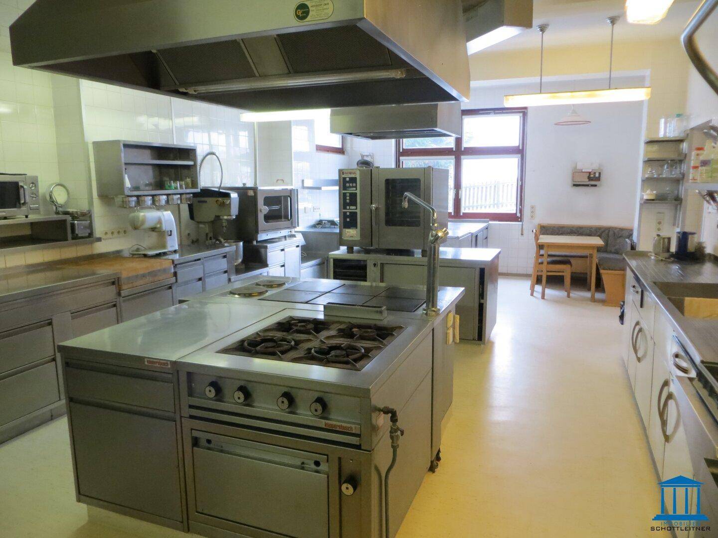 Große Gewerbeküche mit mehreren Kochinseln, Edelstahlgeräten und Ablufthauben für professionelles Kochen.