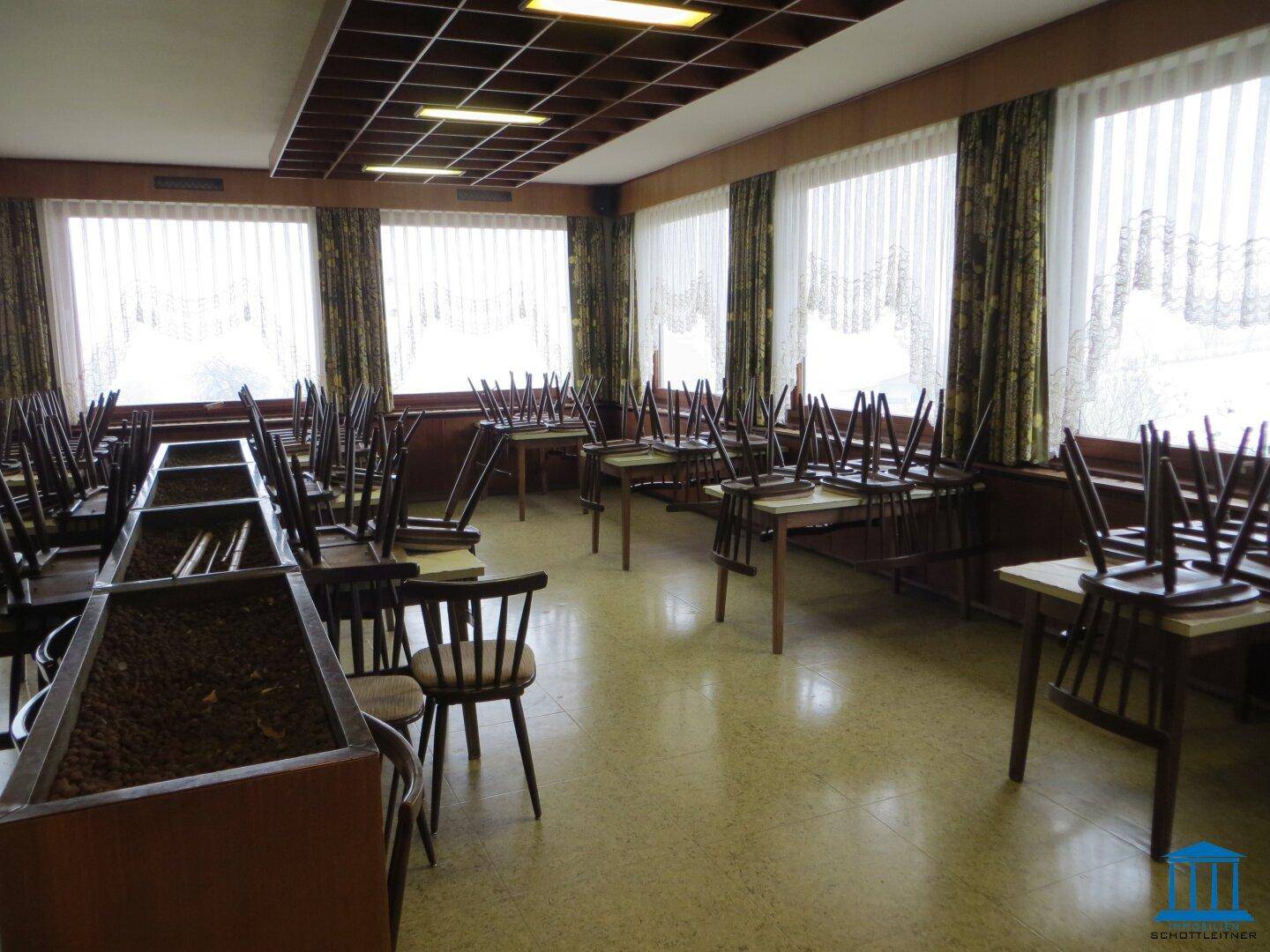 Großer Speisesaal mit vielen Tischen und Stühlen, bereit für Gäste, mit großen Fenstern.