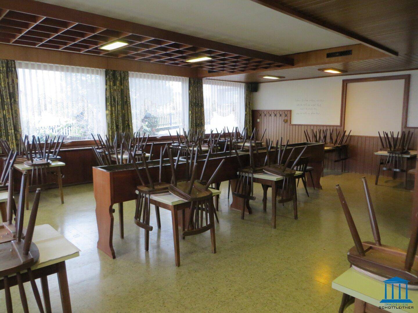 Geräumiger Speisesaal mit Holztischen und Stühlen, großen Fenstern und traditioneller Deckenverkleidung.