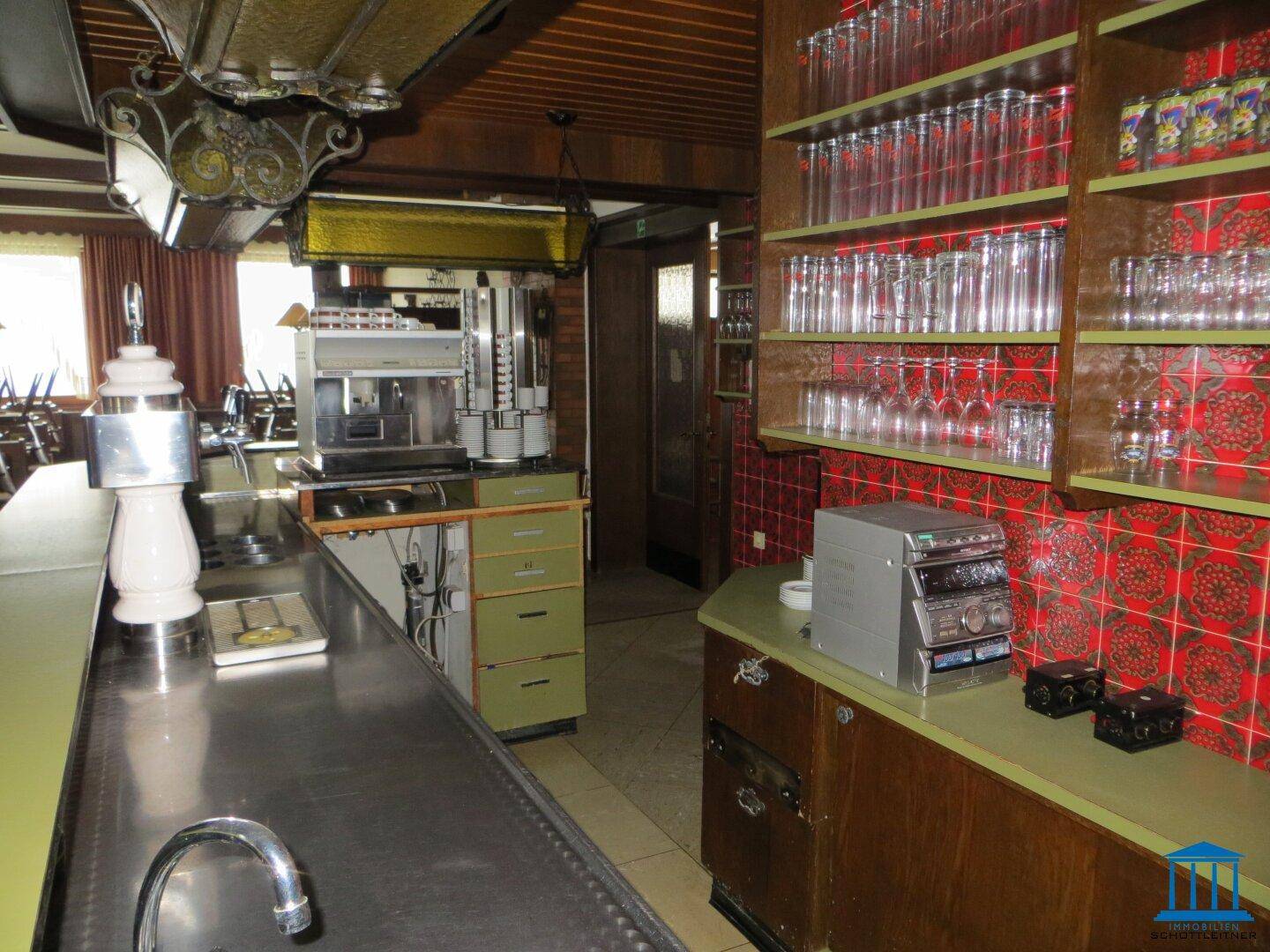 Thekenbereich mit Zapfanlage, Kaffeemaschine und vielen Gläsern, umgeben von Holzvertäfelung und Fliesen.