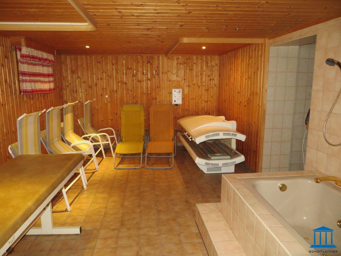 Wellnessbereich mit Holzvertäfelung, Liegestühlen, Solarium und einer eingebauten Badewanne.