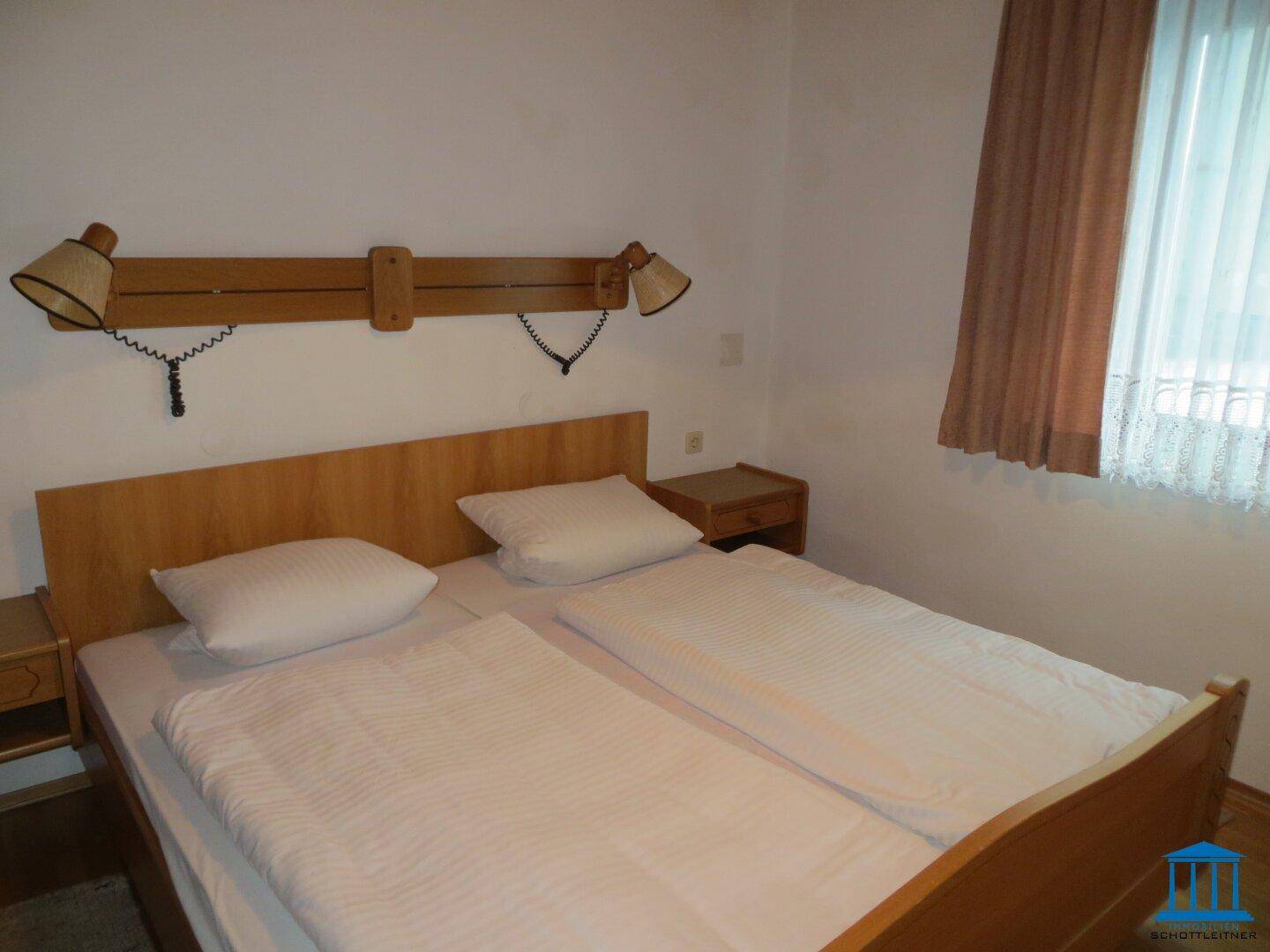 Helles Schlafzimmer mit Doppelbett, Holzmöbeln und einem Fenster mit Vorhängen.