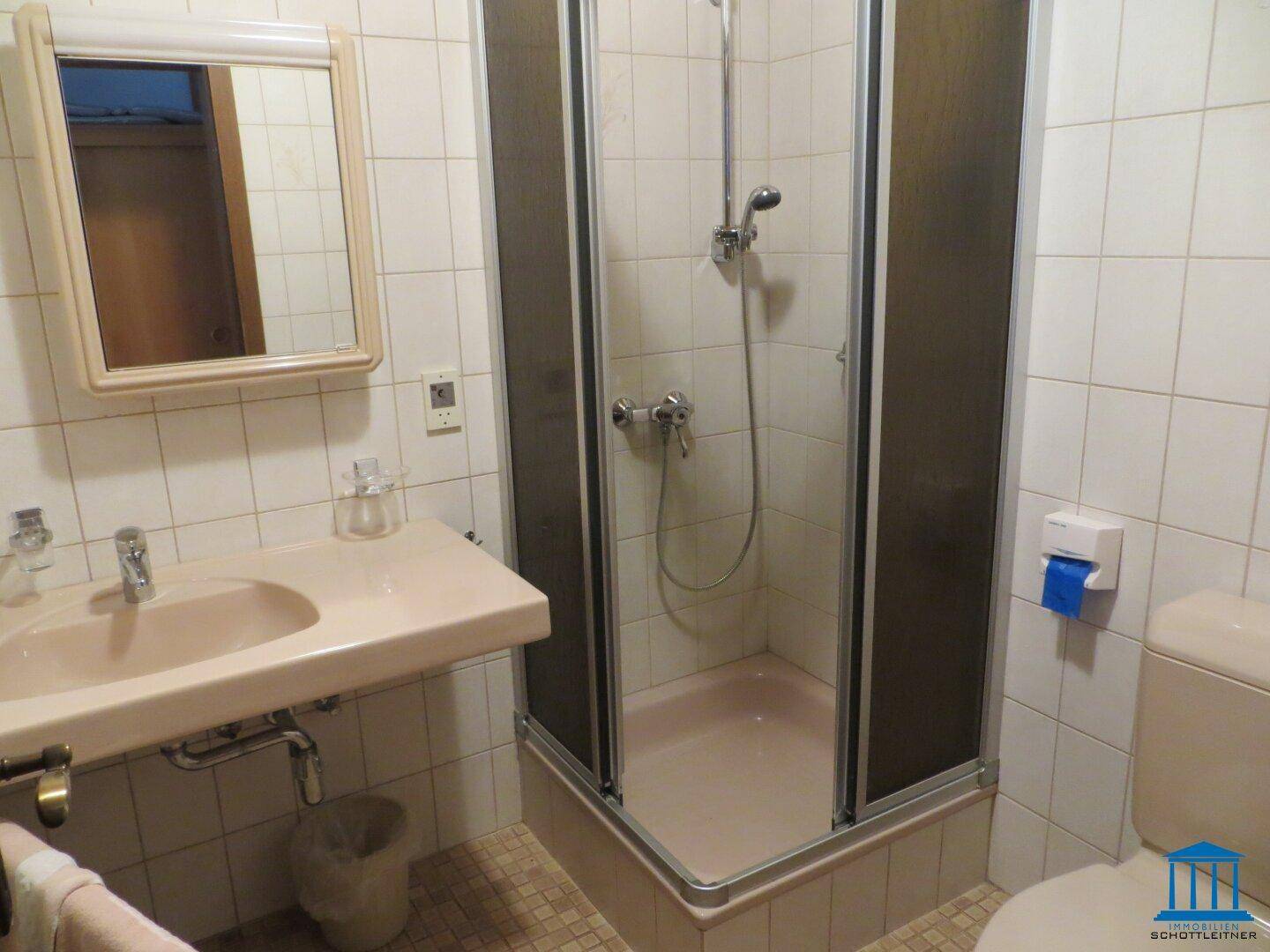 Badezimmer mit Duschkabine, Waschbecken und Toilette, gefliest in hellem Beige.