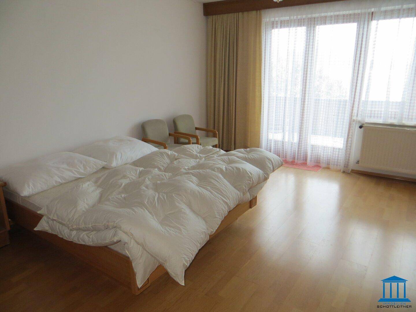 Geräumiges Schlafzimmer mit Doppelbett, hellen Wänden und großem Fenster mit Balkonzugang.