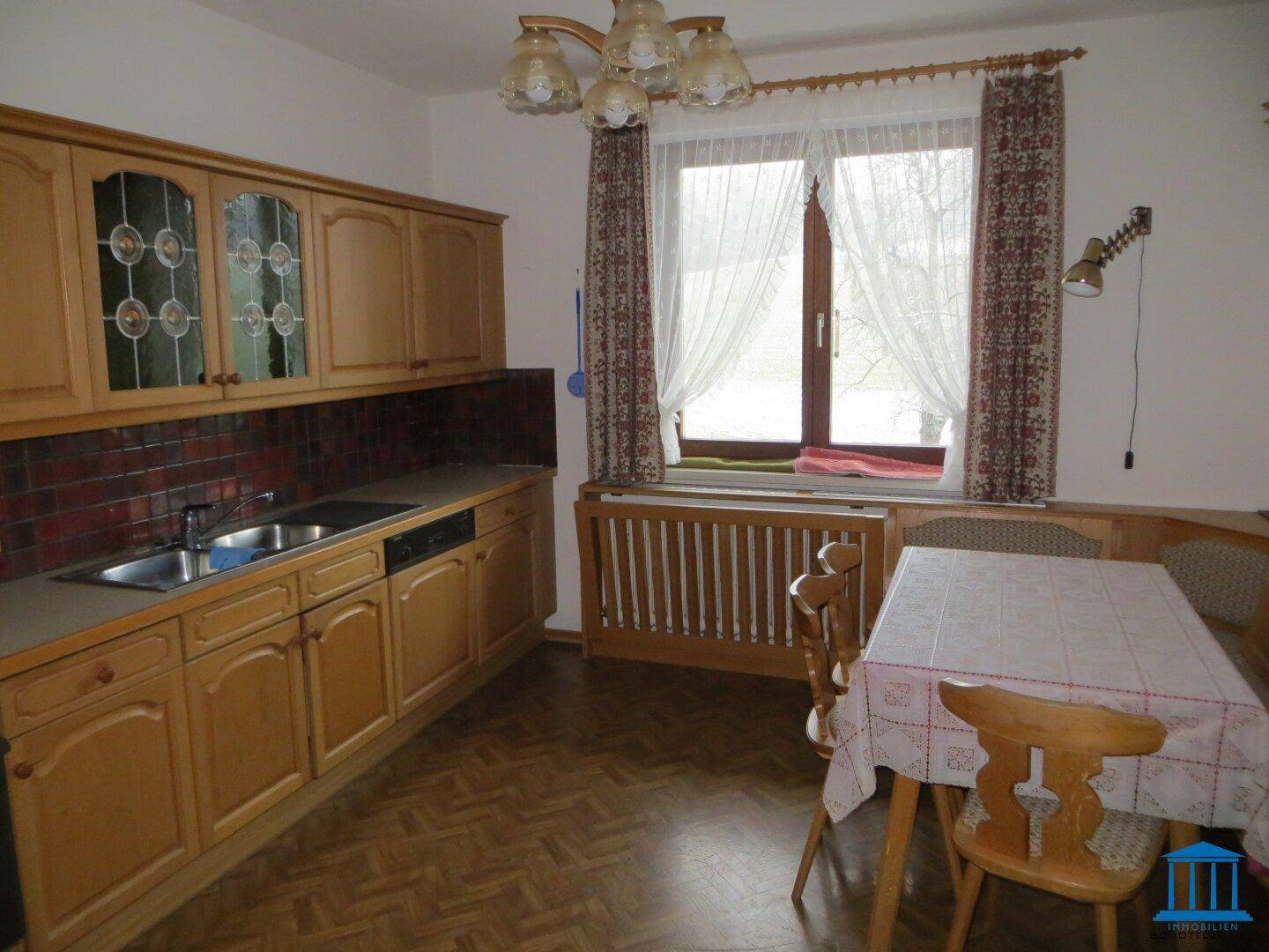 Traditionelle Küche mit Holzeinbauschränken, Esstisch und Fenster mit Vorhängen.