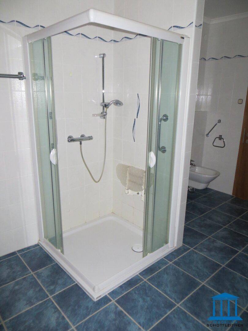 Badezimmer mit Duschkabine, blauen Bodenfliesen und einem Bidet im Hintergrund.
