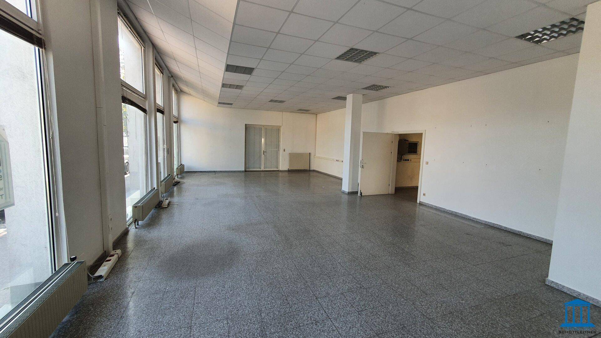 Heller Gewerberaum mit großen Fensterfronten und grauem Fliesenboden, bereit für individuelle Gestaltung.