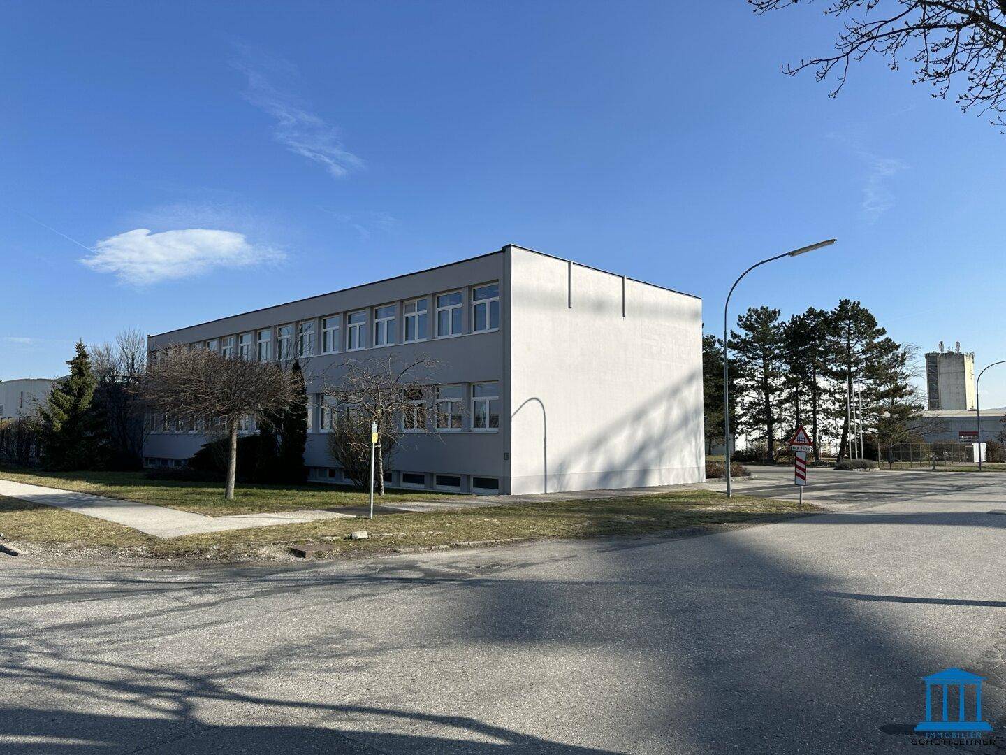Seitenansicht des Bürogebäudes von der Straße aus mit Bäumen und einer Straßenlaterne.