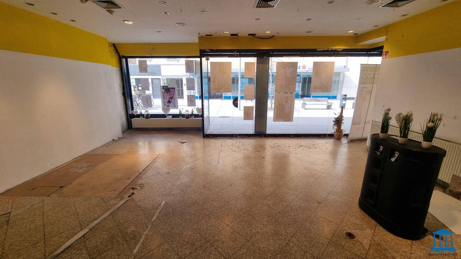 Leerer Ladenraum mit großen Schaufenstern zur Straße und Fliesenboden, bereit für den Ausbau.