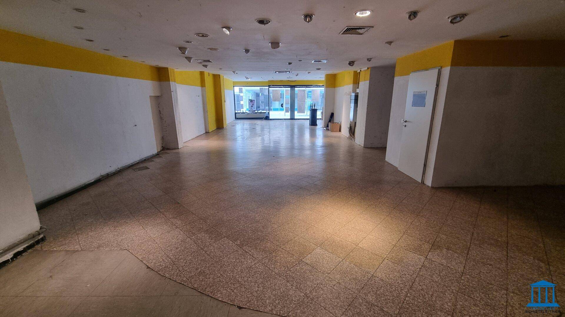 Weitläufiger Ladenbereich mit Fliesenboden und Blick auf die großen Schaufenster zur Straße.