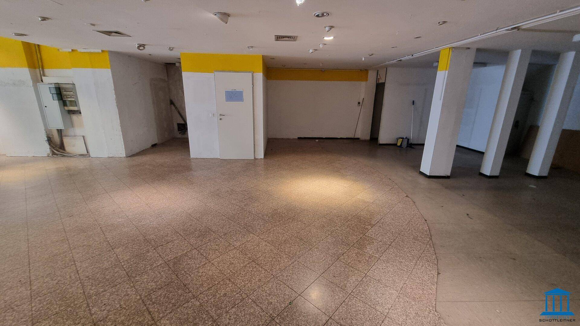 Großer Ladenraum mit Fliesenboden und Zugang zu weiteren Räumen, ideal für verschiedene Geschäftskonzepte.