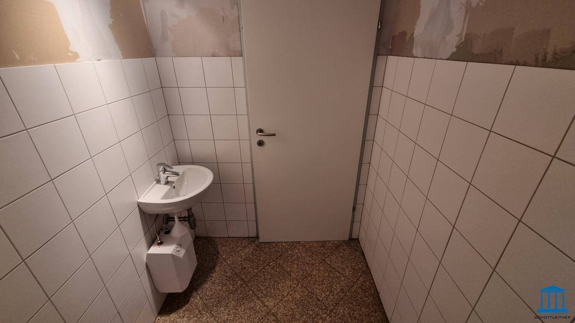 Kleine Toilette mit Waschbecken und weißen Fliesen an den Wänden, funktional und sauber.