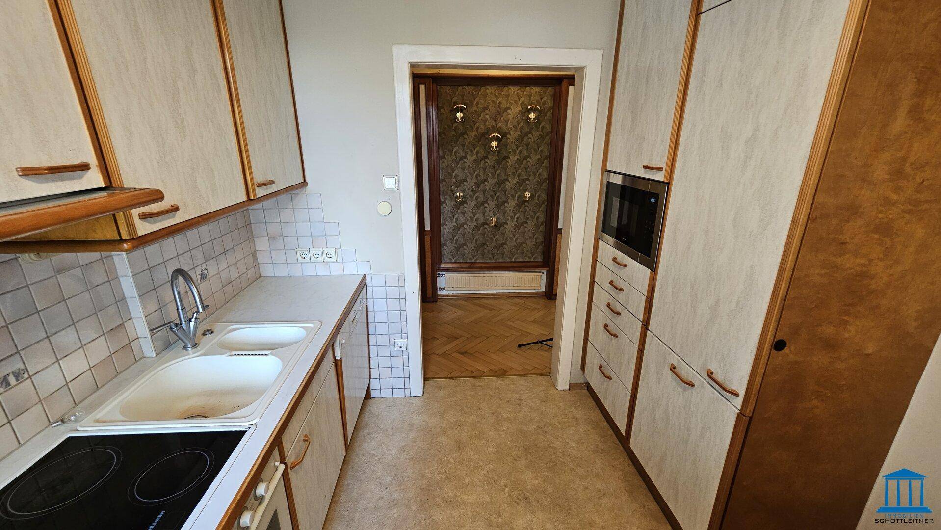Gut ausgestattete Küche mit Einbauschränken, Spüle und Blick auf den angrenzenden Flur.