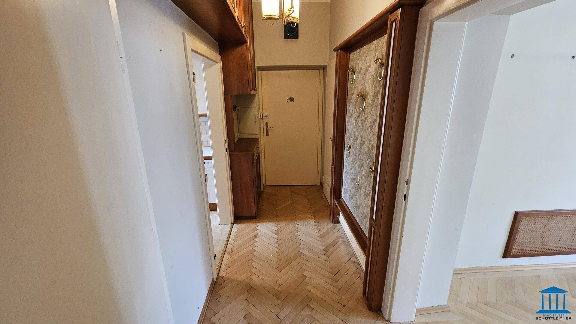 Eingangsbereich mit Fischgrätparkett und einer Garderobe, die zu weiteren Räumen führt.