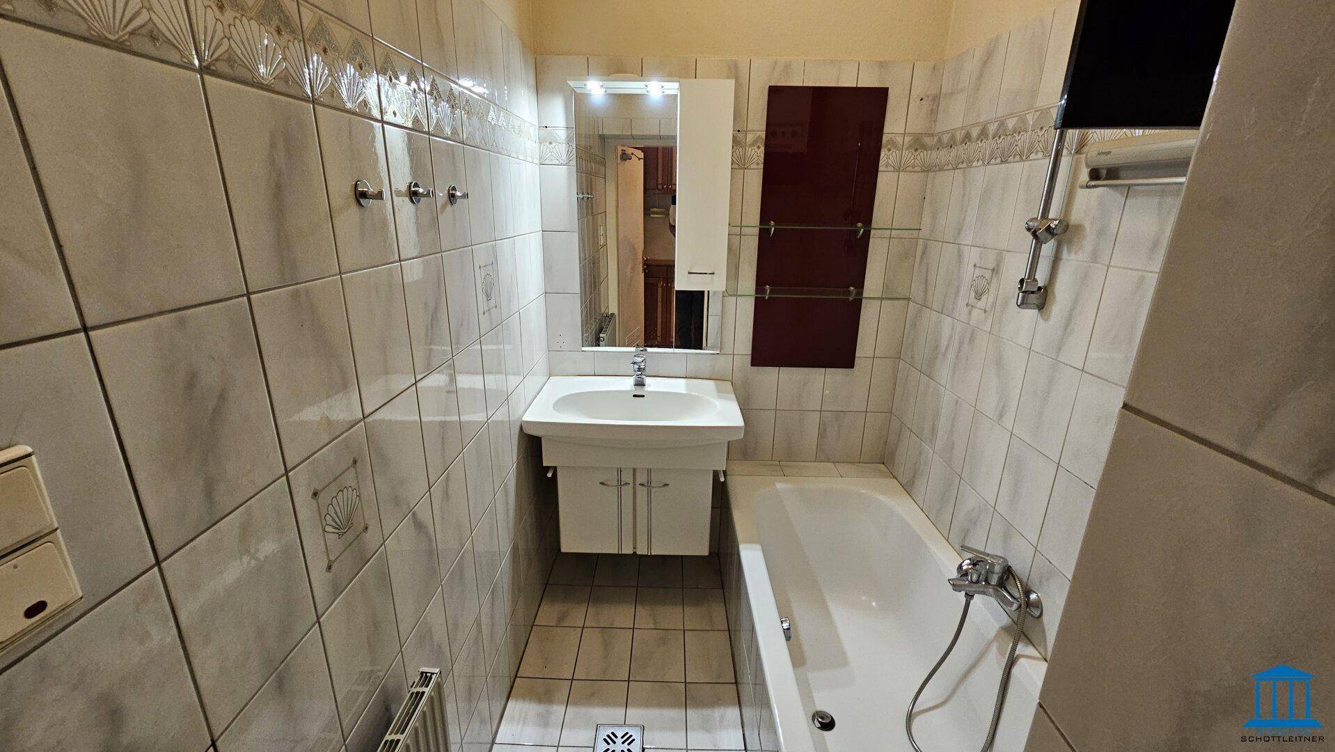 Gefliestes Badezimmer mit Badewanne, Waschbecken und Spiegel, in einem traditionellen Stil gehalten.