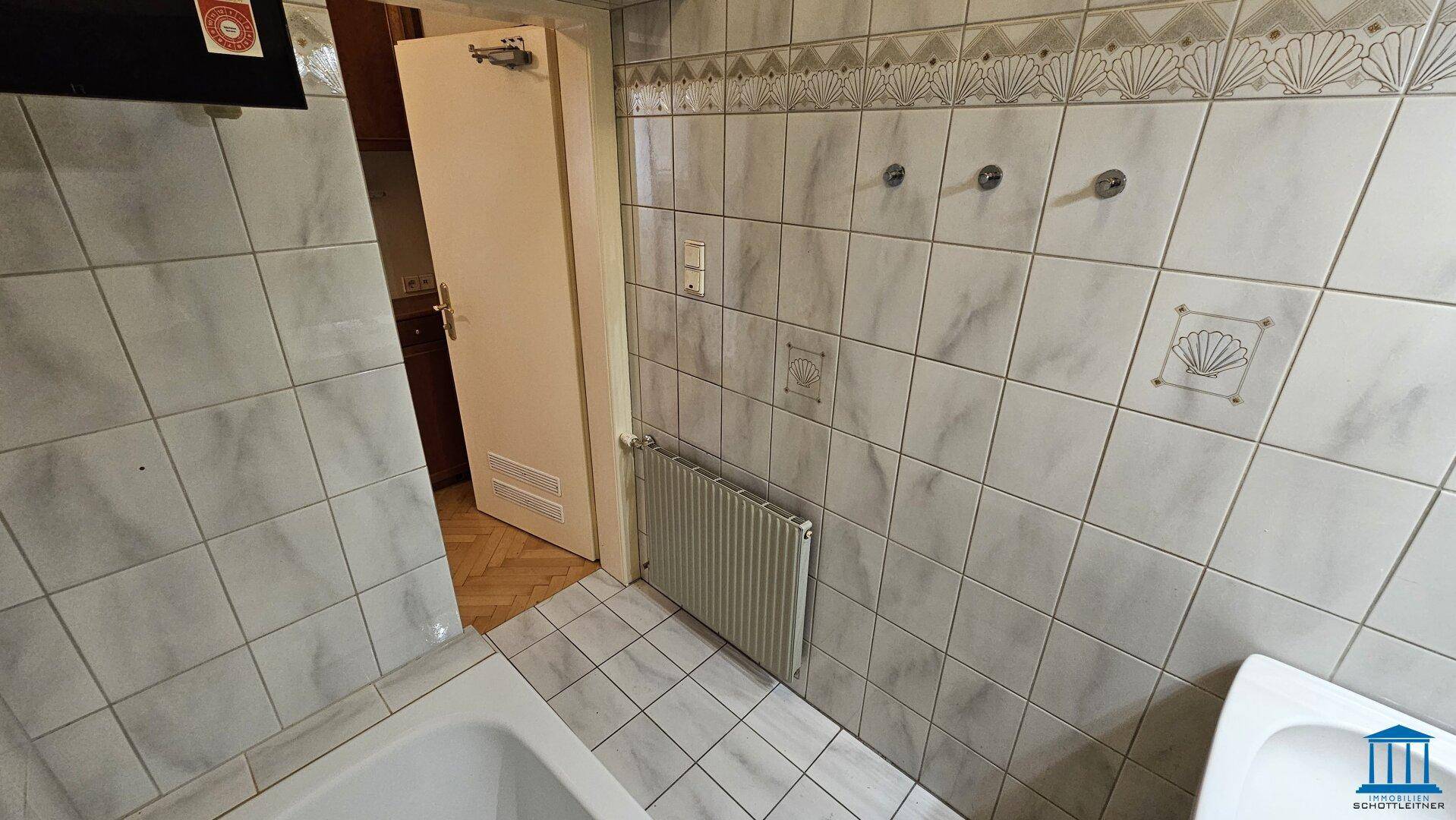 Gefliestes Badezimmer mit Badewanne und Heizkörper, in einem gepflegten Zustand.