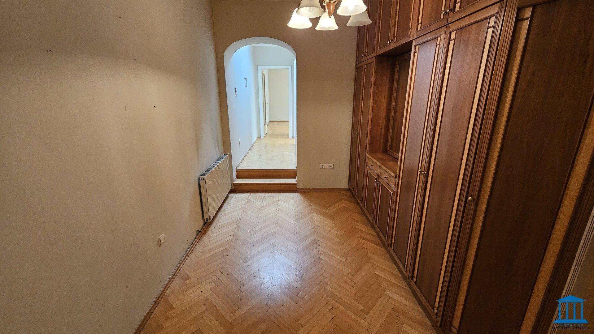 Schlafzimmer mit großem Einbauschrank, Fischgrätparkett und einem kleinen Absatz im Raum.