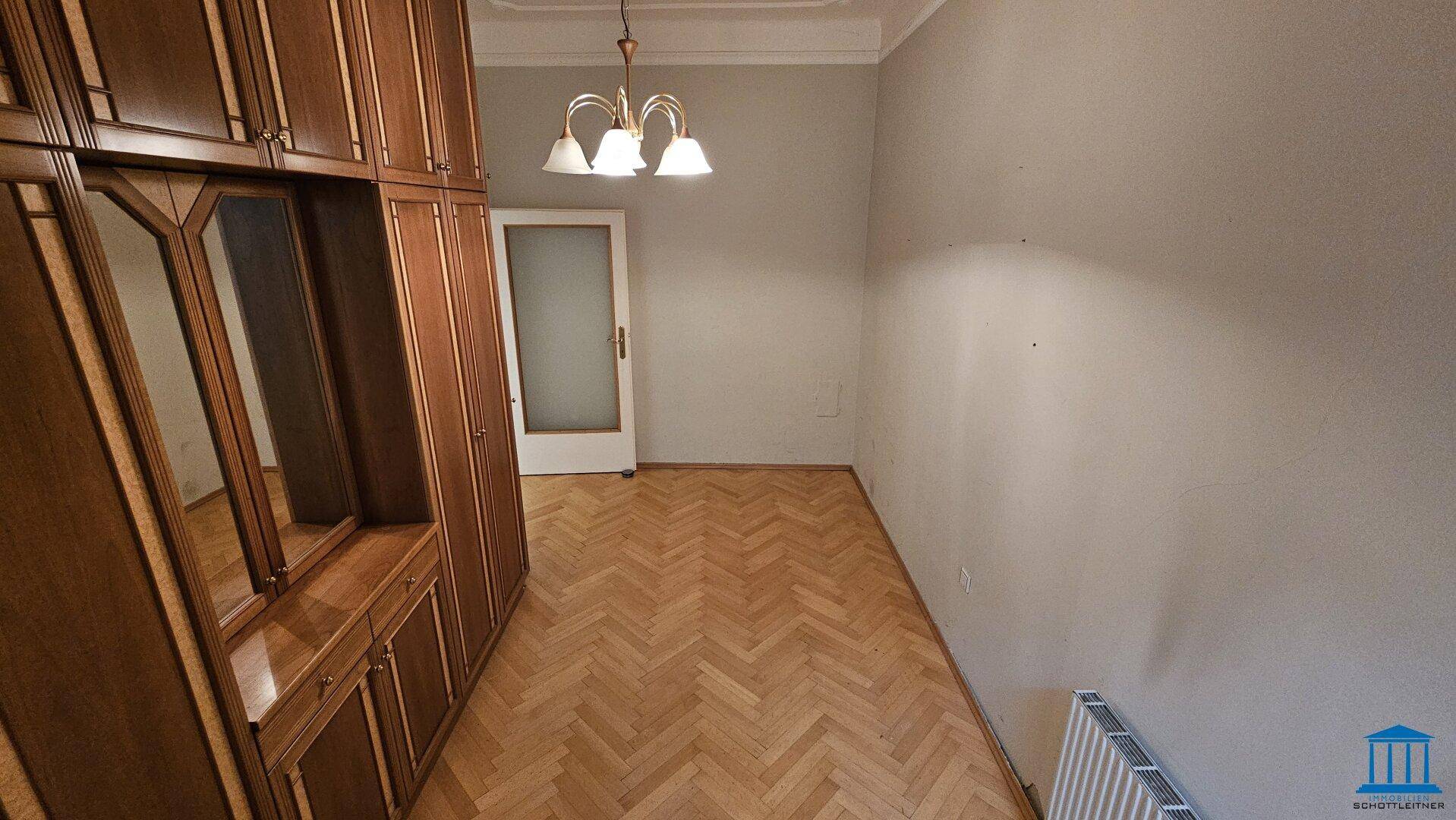Geräumiges Schlafzimmer mit Einbauschränken, Fischgrätparkett und einem Fenster für natürliches Licht.
