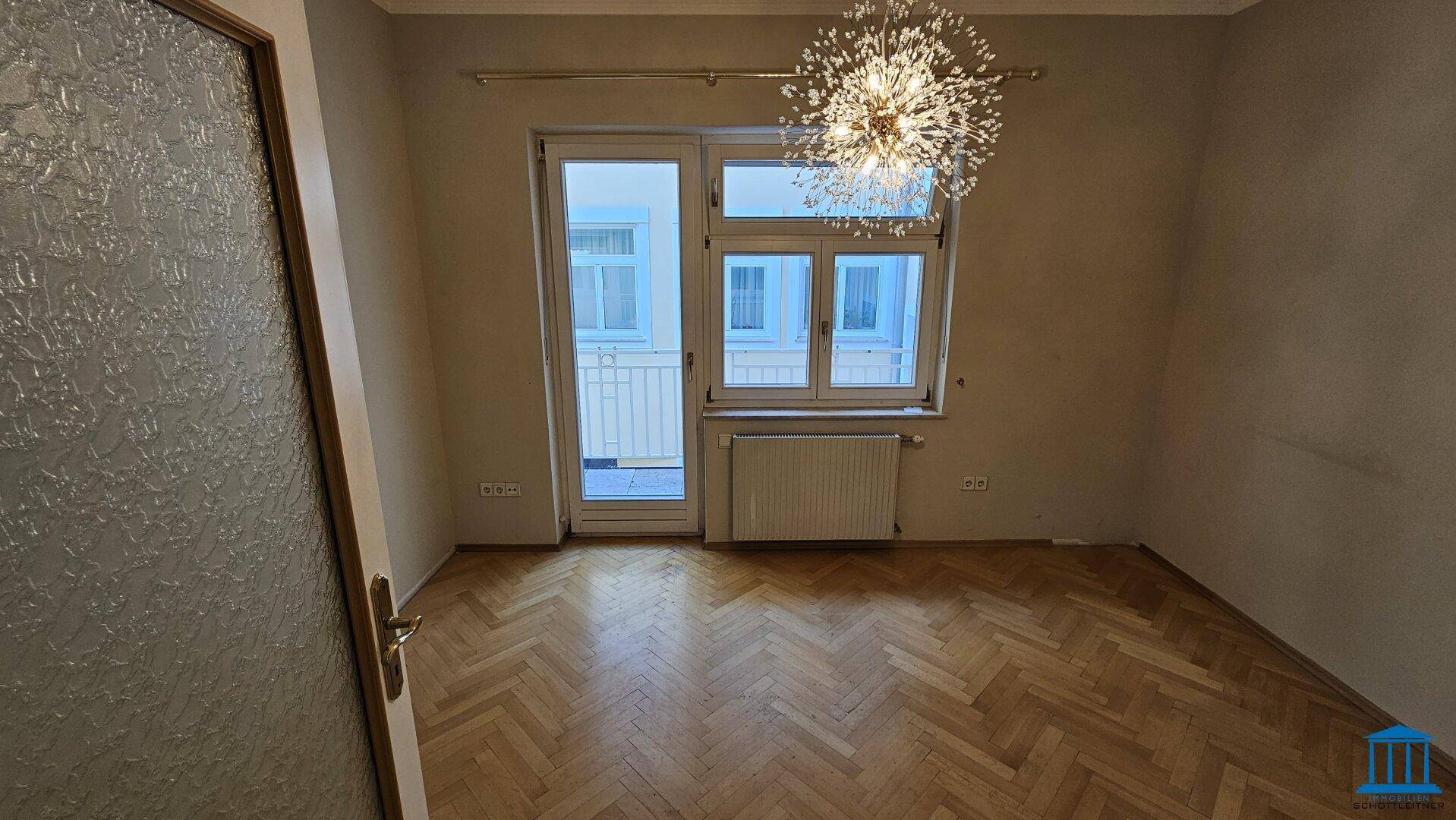 Helles Wohnzimmer mit Fischgrätparkett, moderner Deckenleuchte und Zugang zum Außenbereich.