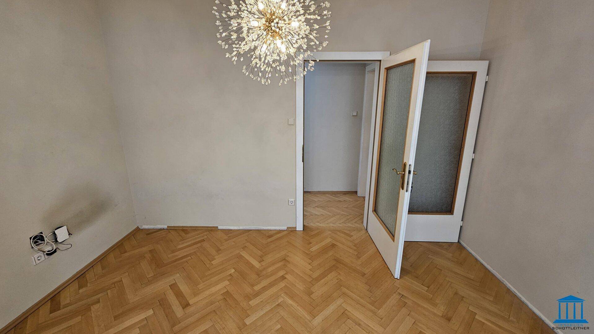 Leeres Wohnzimmer mit Fischgrätparkett und Doppeltüren, die zu einem weiteren Raum führen.