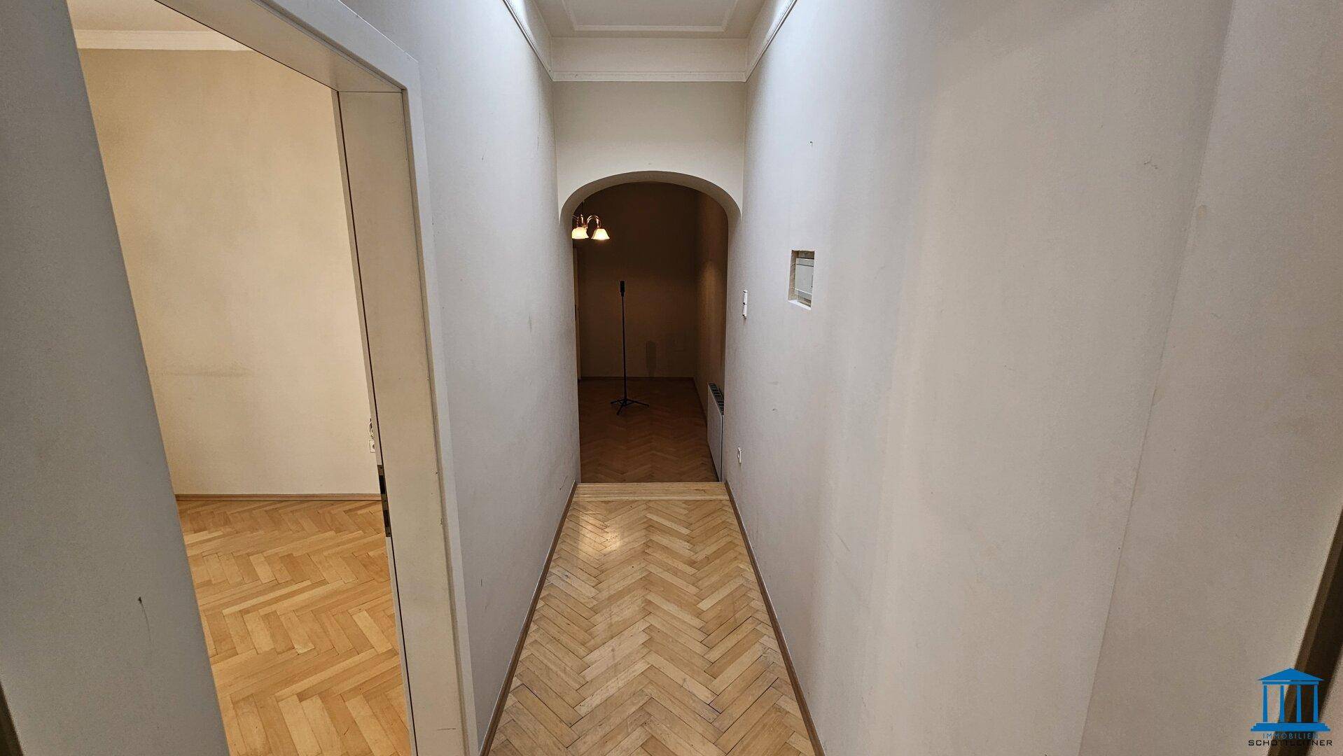 Heller Flur mit Fischgrätparkett und einem eleganten Bogen, der den Übergang zu einem anderen Bereich markiert.