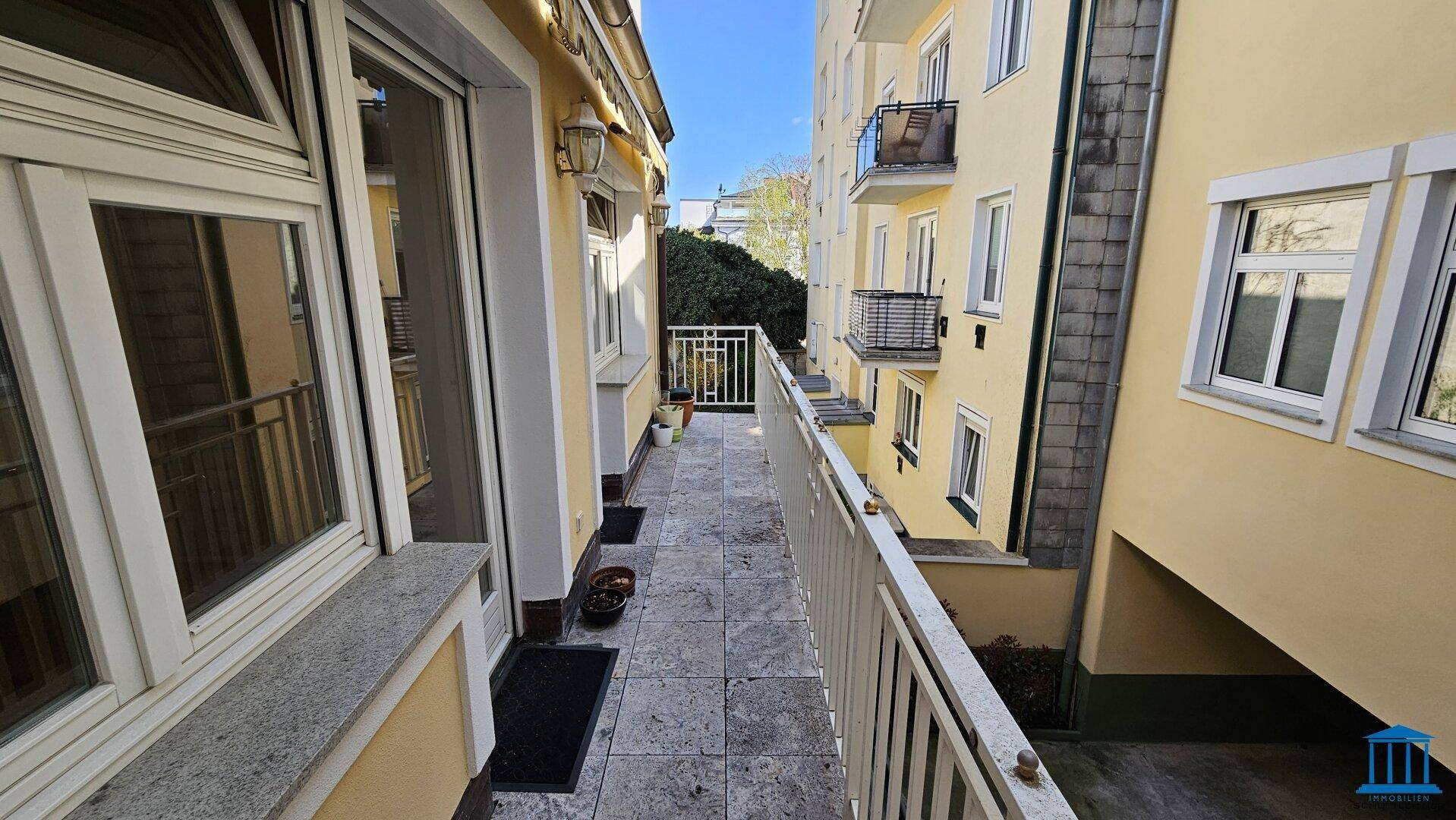 Schmaler Balkon mit Fliesenboden und Metallgeländer, umgeben von Gebäudefassaden.