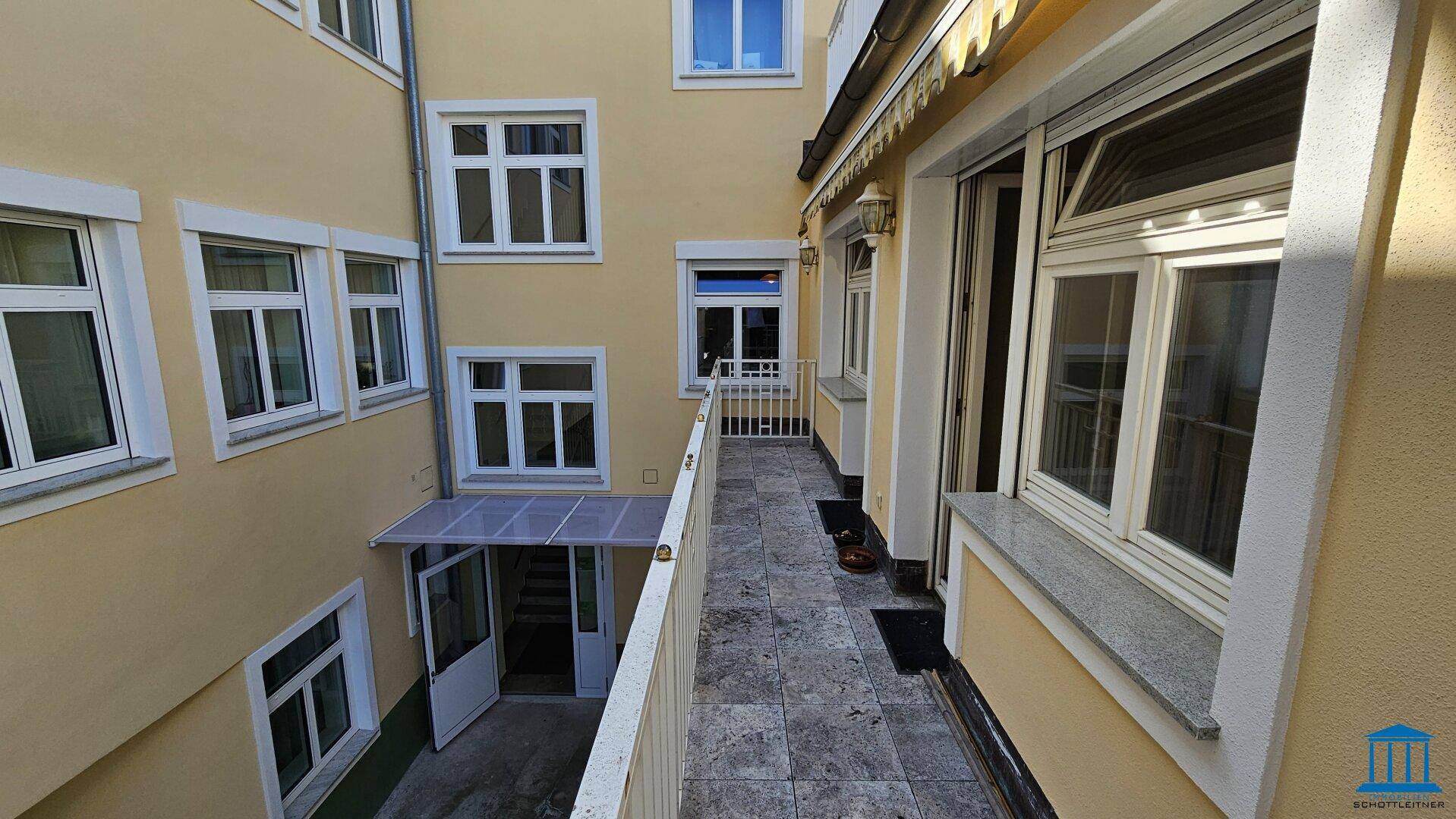 Langer, schmaler Balkon mit Fliesenboden und Blick auf den Innenhof des Gebäudekomplexes.