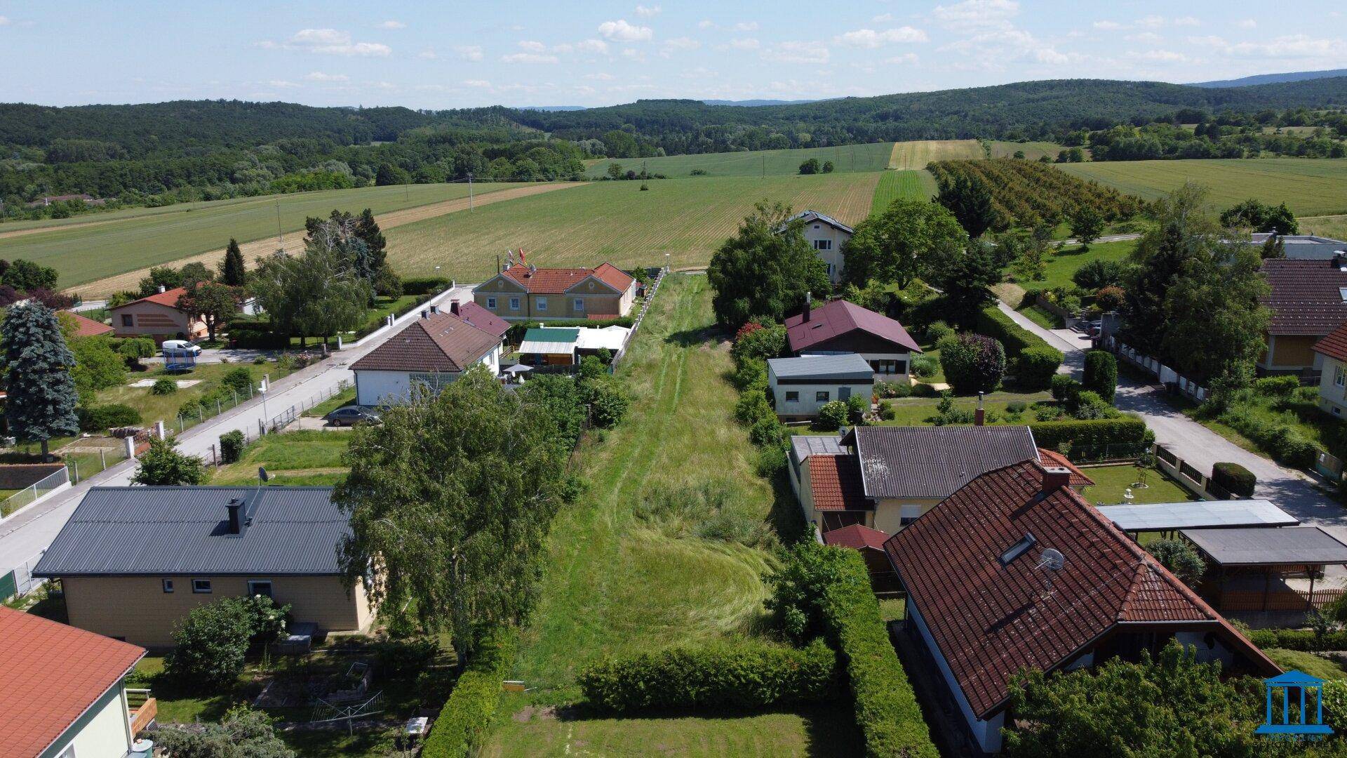 Weitläufige Luftaufnahme eines ländlichen Wohngebiets mit Feldern und Wäldern im Hintergrund.