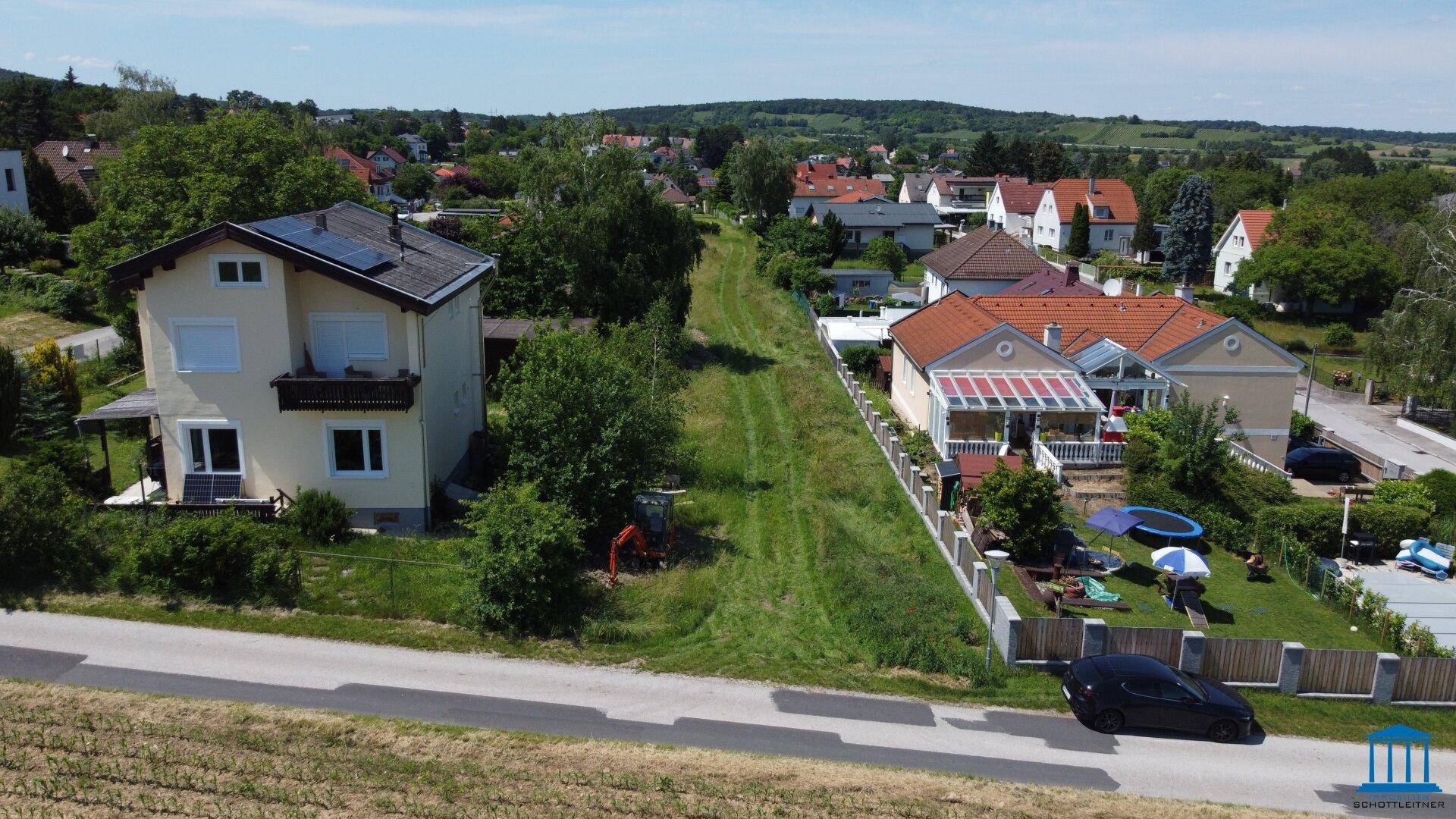 Luftaufnahme eines Wohngebiets mit Häusern, Gärten und einer Straße unter blauem Himmel.